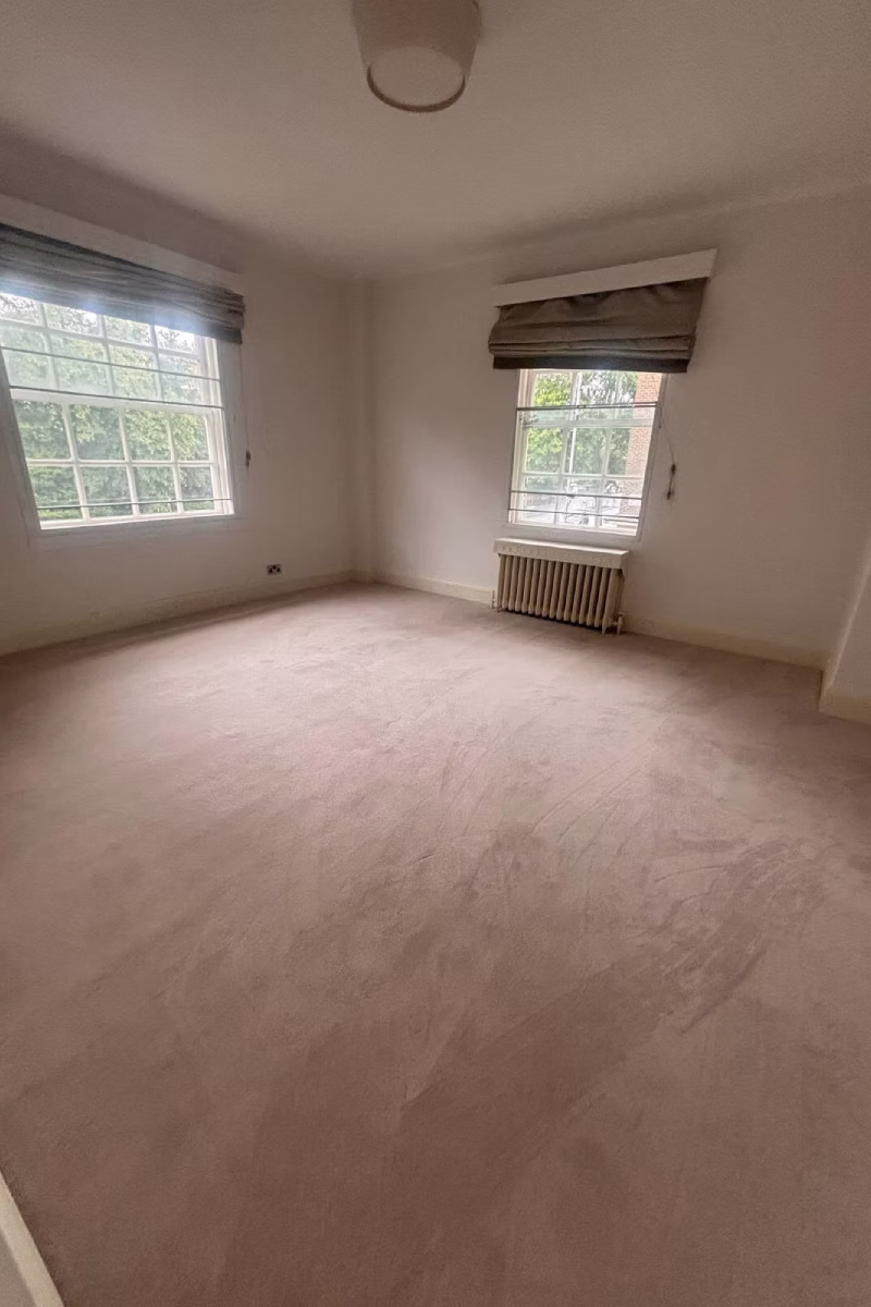 An empty room featuring beige wall-to-wall carpet, two windows with blinds, and white walls.